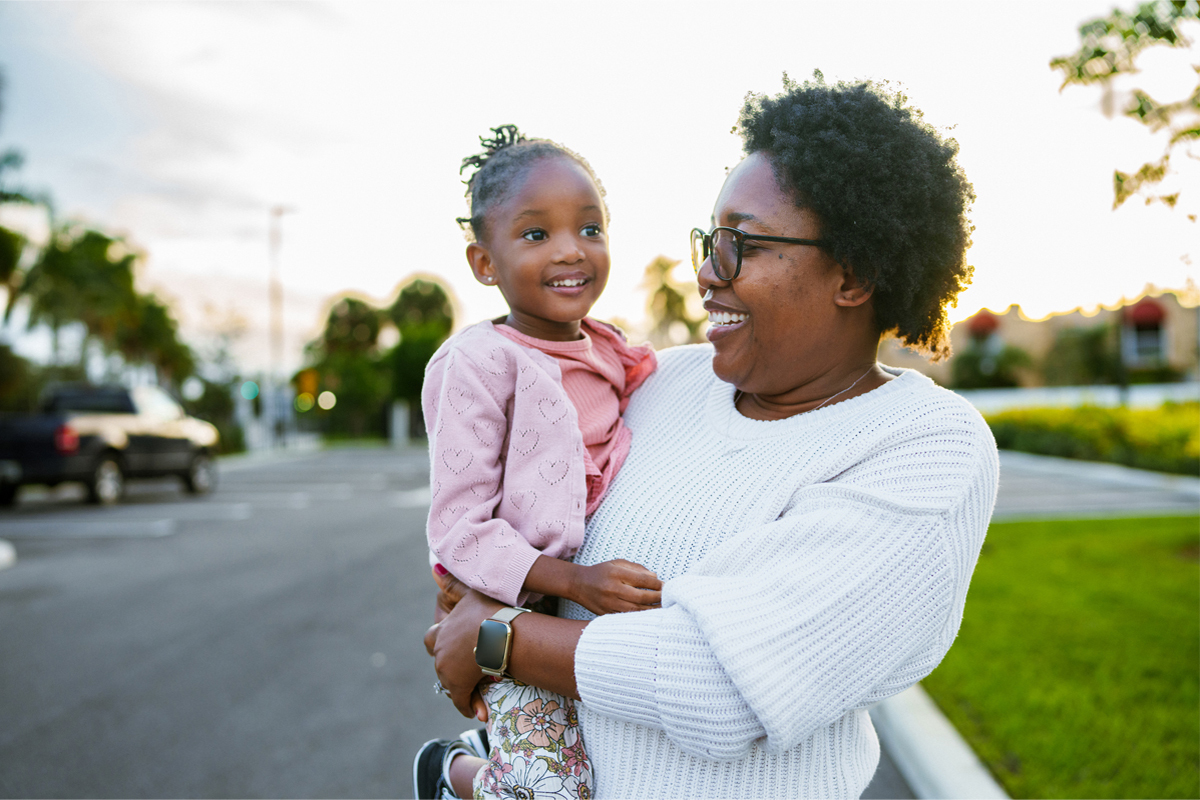 Woman holding child outside.